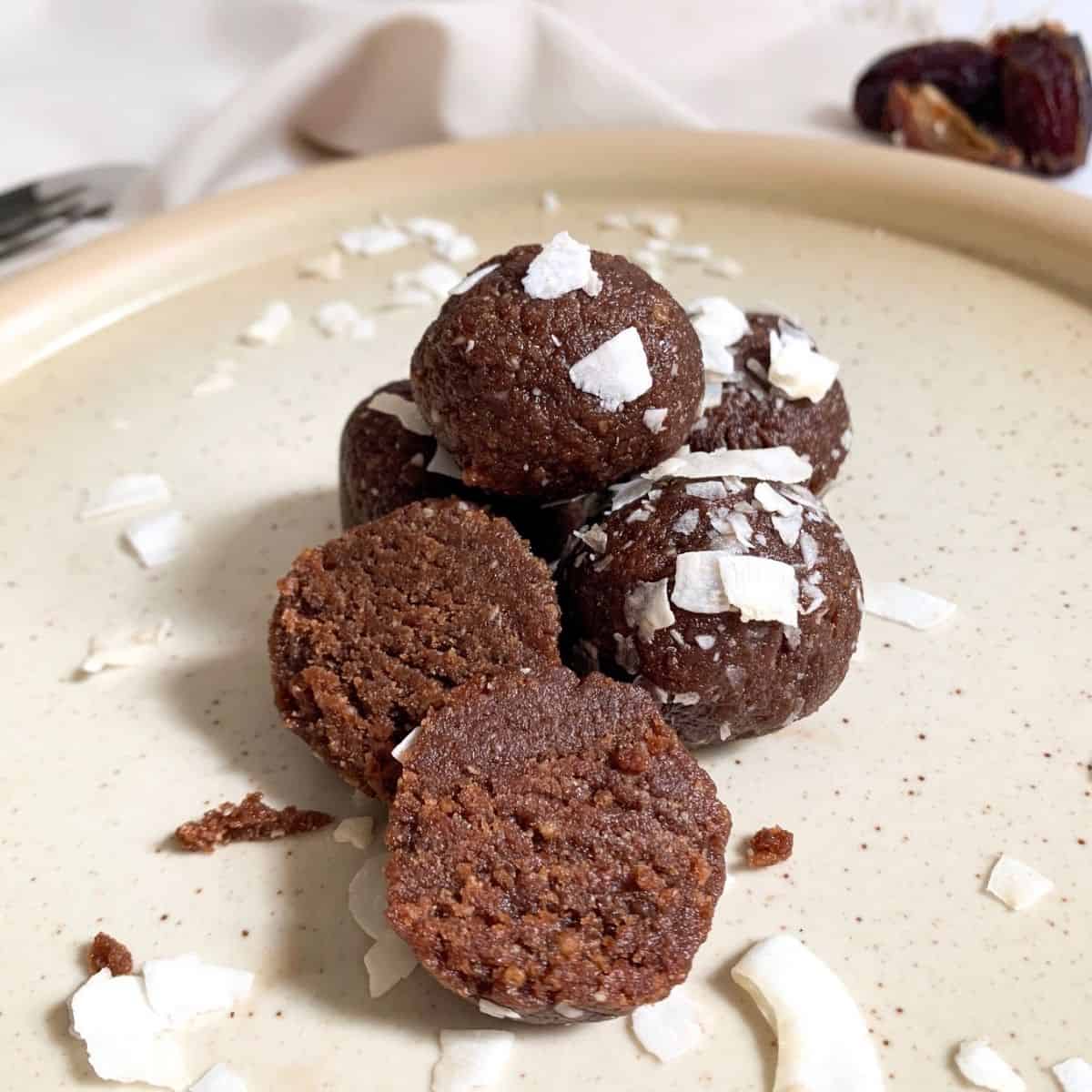 chocolate coconut date balls in a pile with one cut in half to see the inside texture