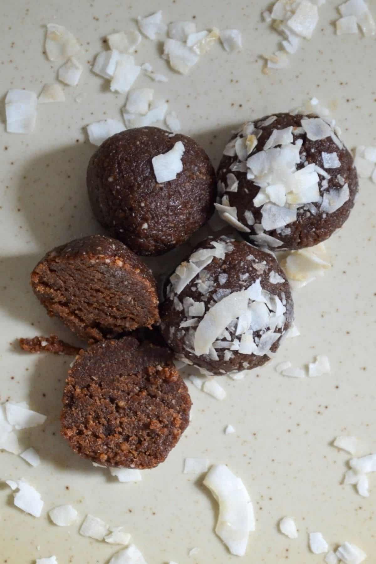 chocolate coconut date balls with one split in half and topped with coconut chips