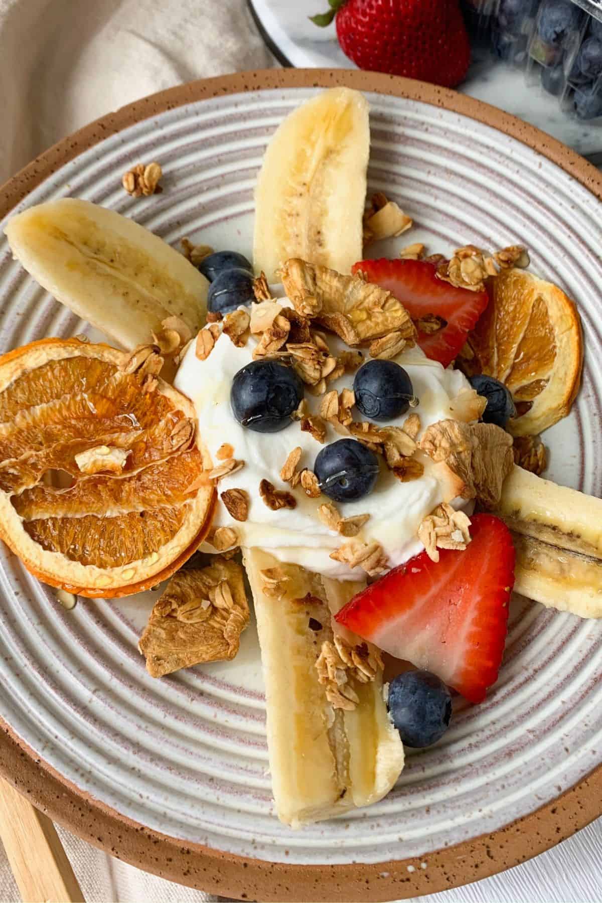 yogurt banana split topped with fresh fruit, dried fruit and granola