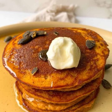 stack of pumpkin protein pancakes topped with greek yogurt, pumpkin seeds and maple syrup