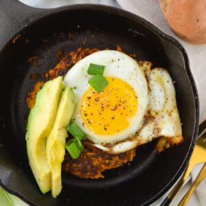 sweet potato hash topped with a sunny side egg and avocado slices
