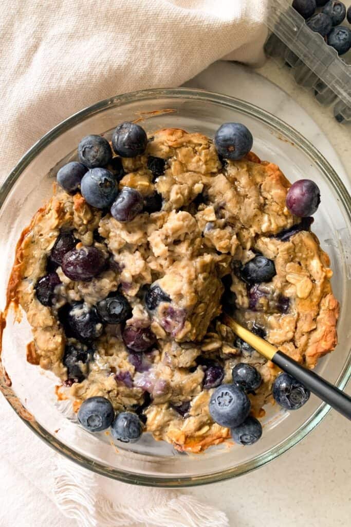 blueberry muffin baked oats in a glass bowl topped with blueberries