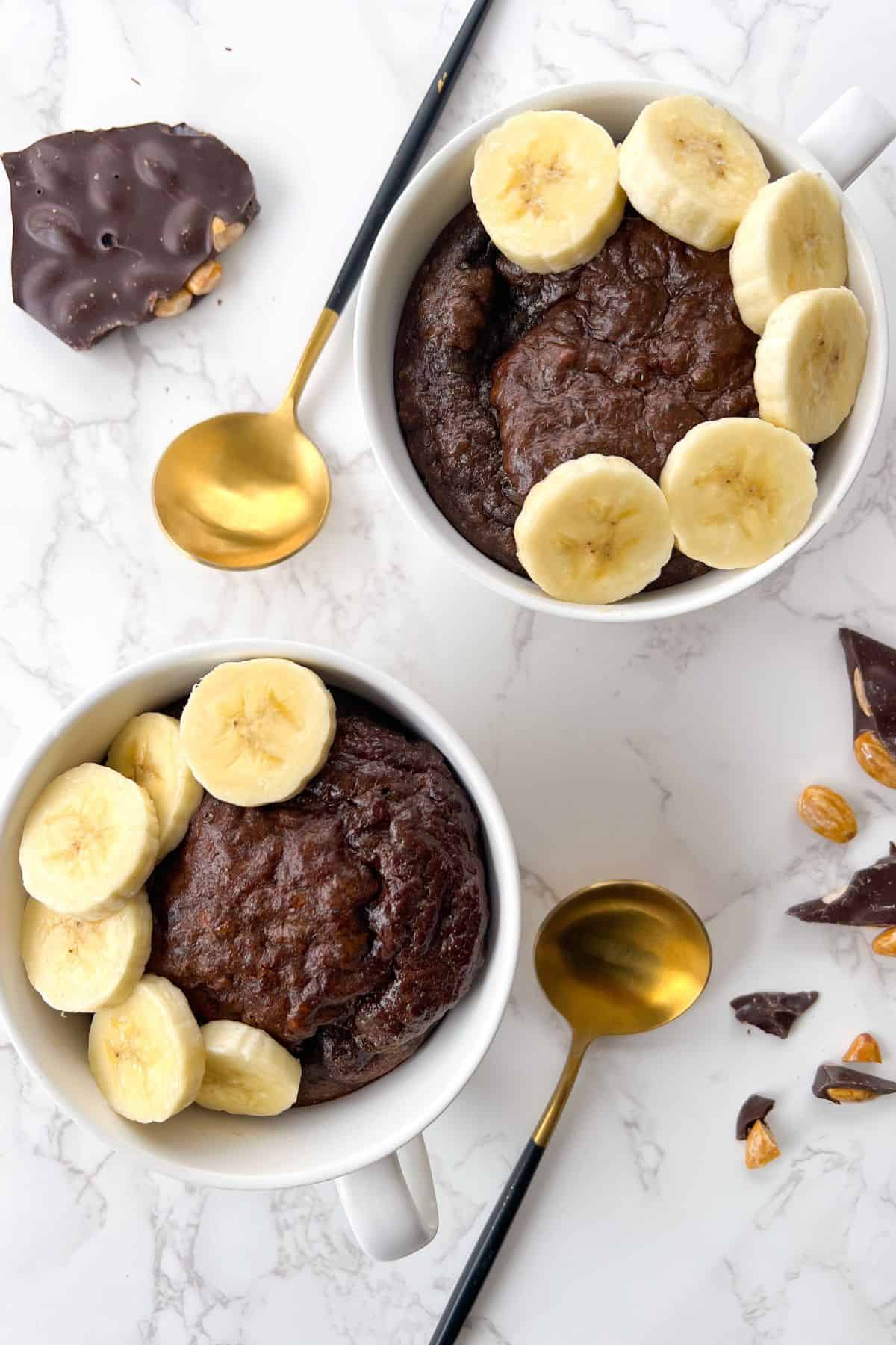 two chocolate protein mug cakes next to each other and topped with banana slices