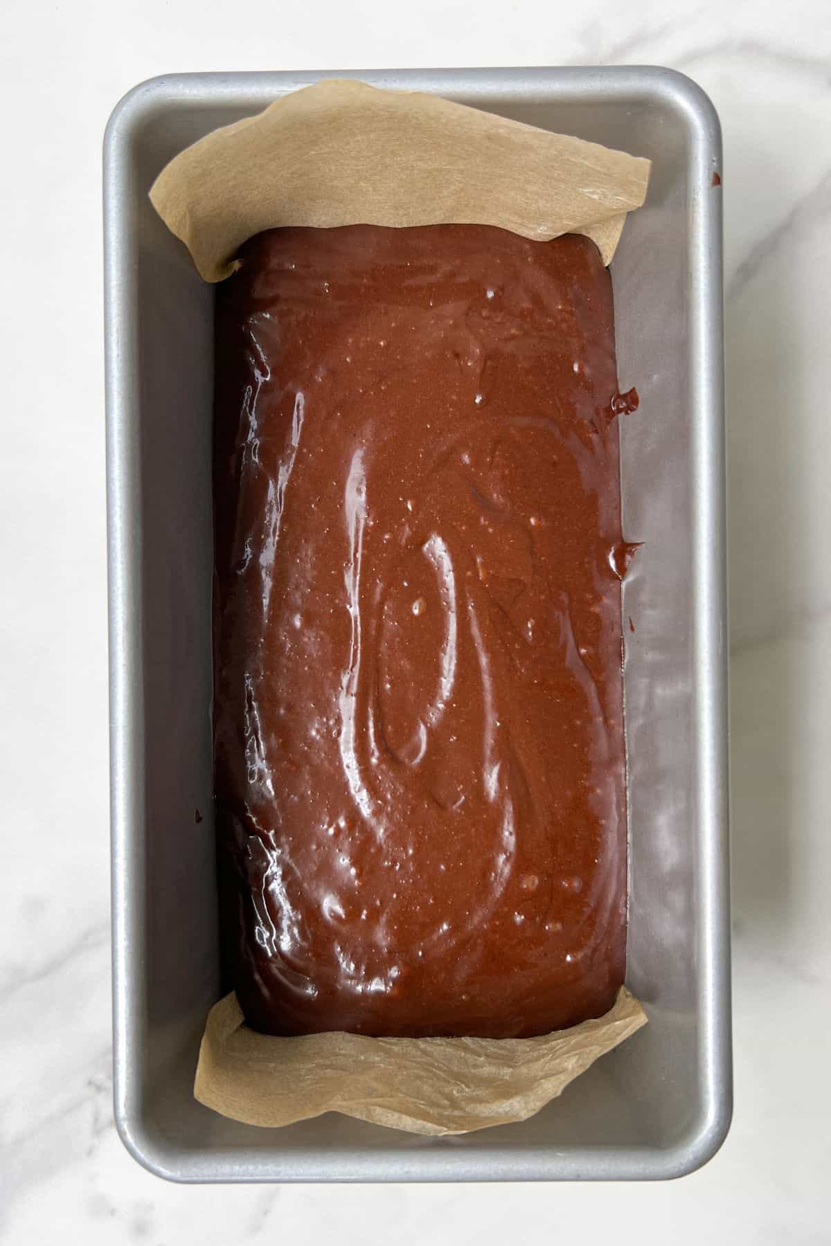 Mini Chocolate Cake batter in a loaf pan lined with parchment paper.