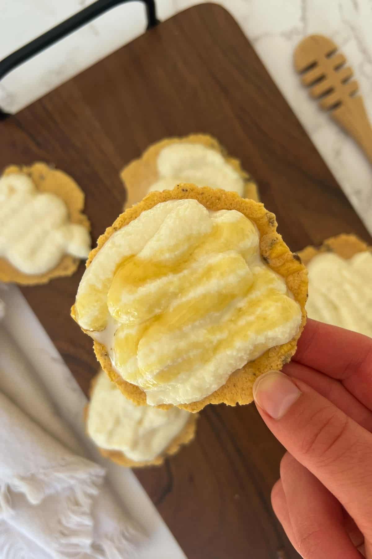holding a cracker with the spread on top and an extra honey drizzle