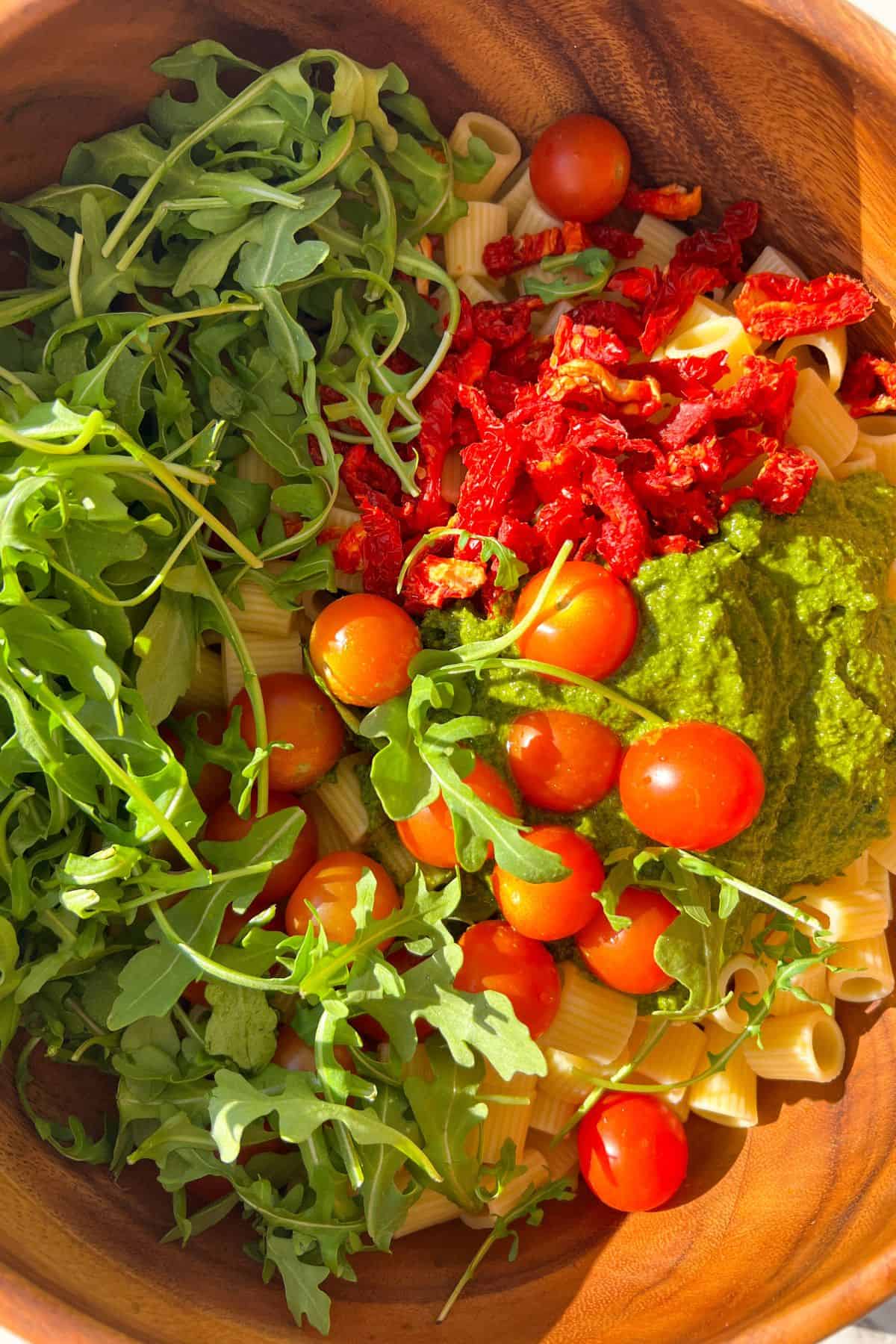 Making Pesto Pasta Salad in a large bowl.