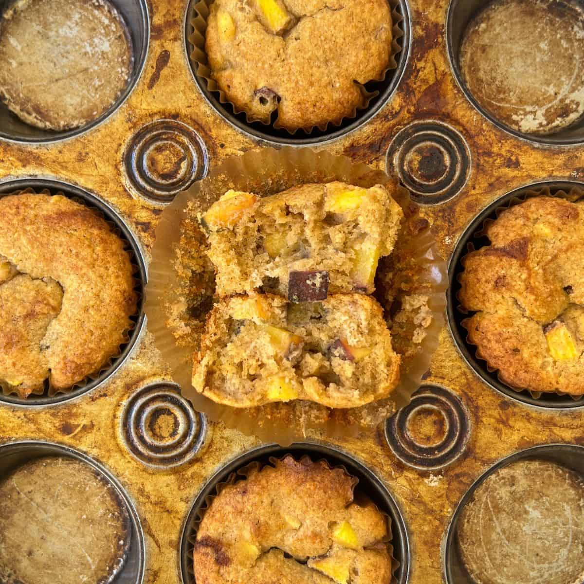 peach muffin split open on top of the muffin pan