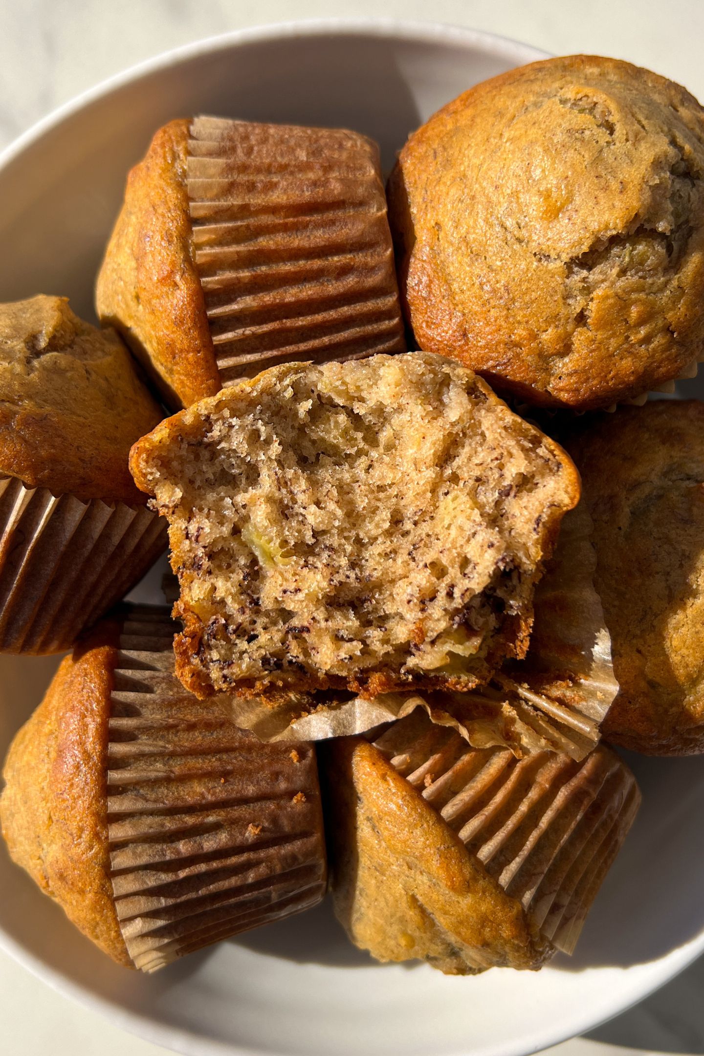 Banana muffins in a platter with one broken in half to show the inside texture.