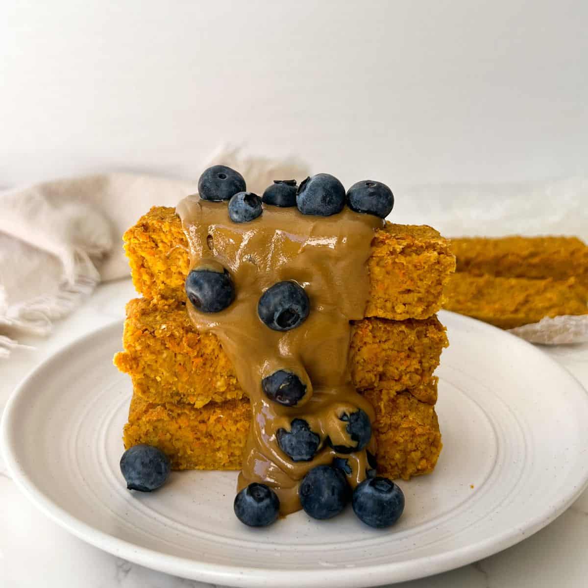 3 carrot cake oatmeal bars stacked and topped with sunflower butter and fresh blueberries