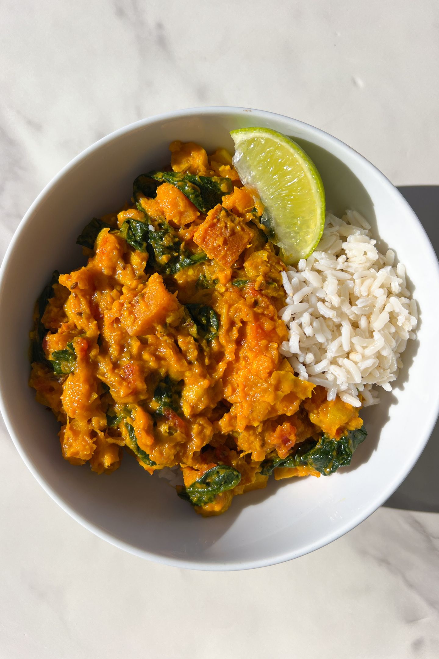 Sweet Potato Spinach and Chickpea Curry in a bowl with rice and slice of lime.