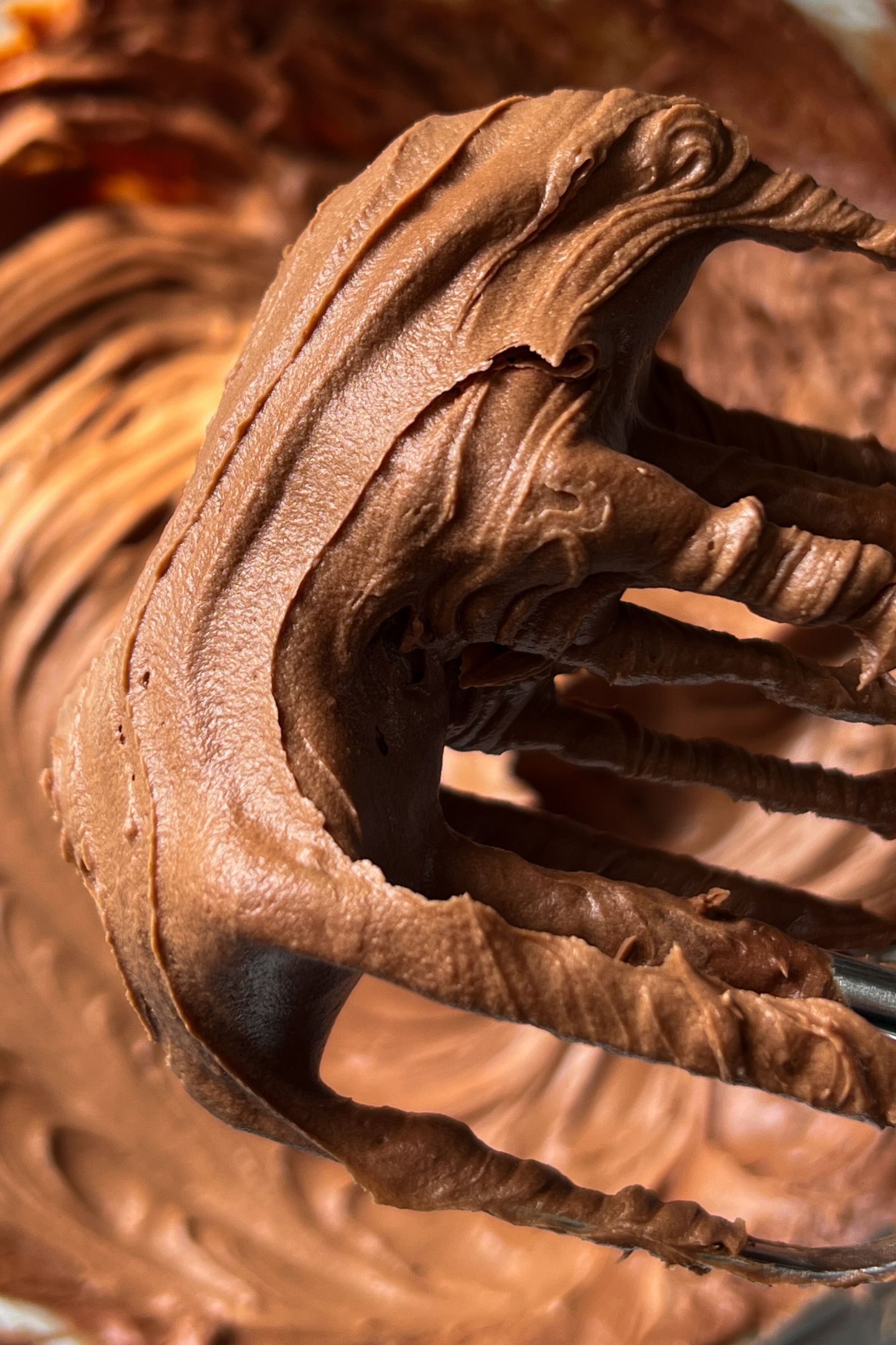 Whipped chocolate frosting in bowl on the whisk attachments.