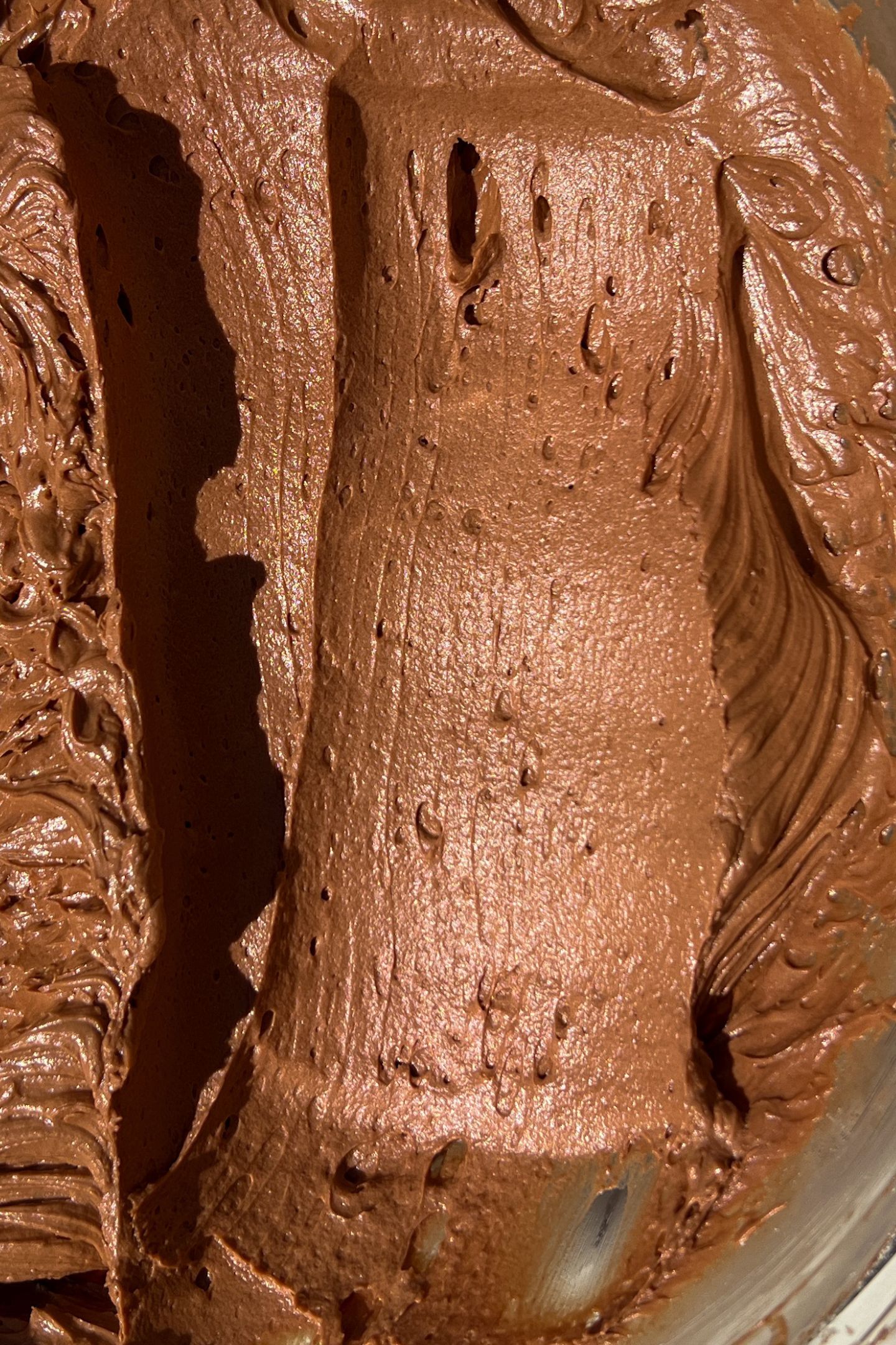 Chocolate frosting in a bowl with a scoop taken out of it.