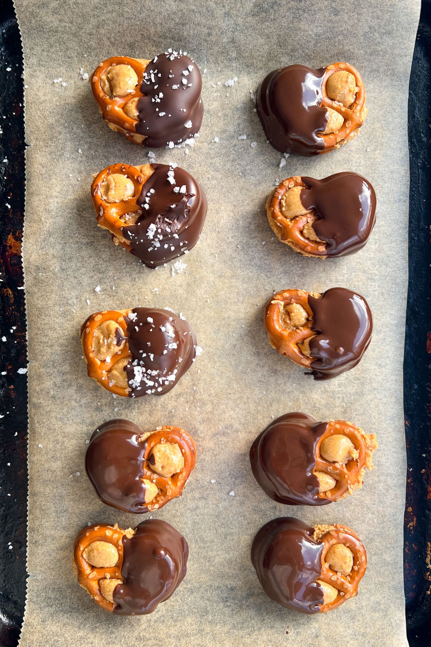 Dipped peanut butter pretzels on baking sheet topped with flake sea salt.