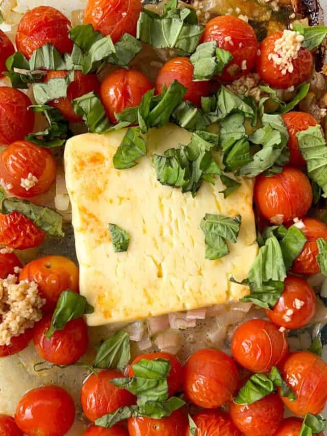 baked feta in a tray with tomatoes, shallots, garlic and fresh basil.