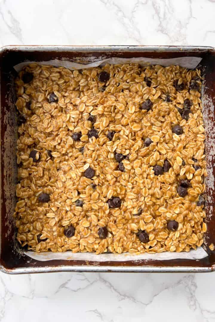 No Bake Chocolate Oat Bars pressed into a 8x8 baking pan topped with chocolate chips.