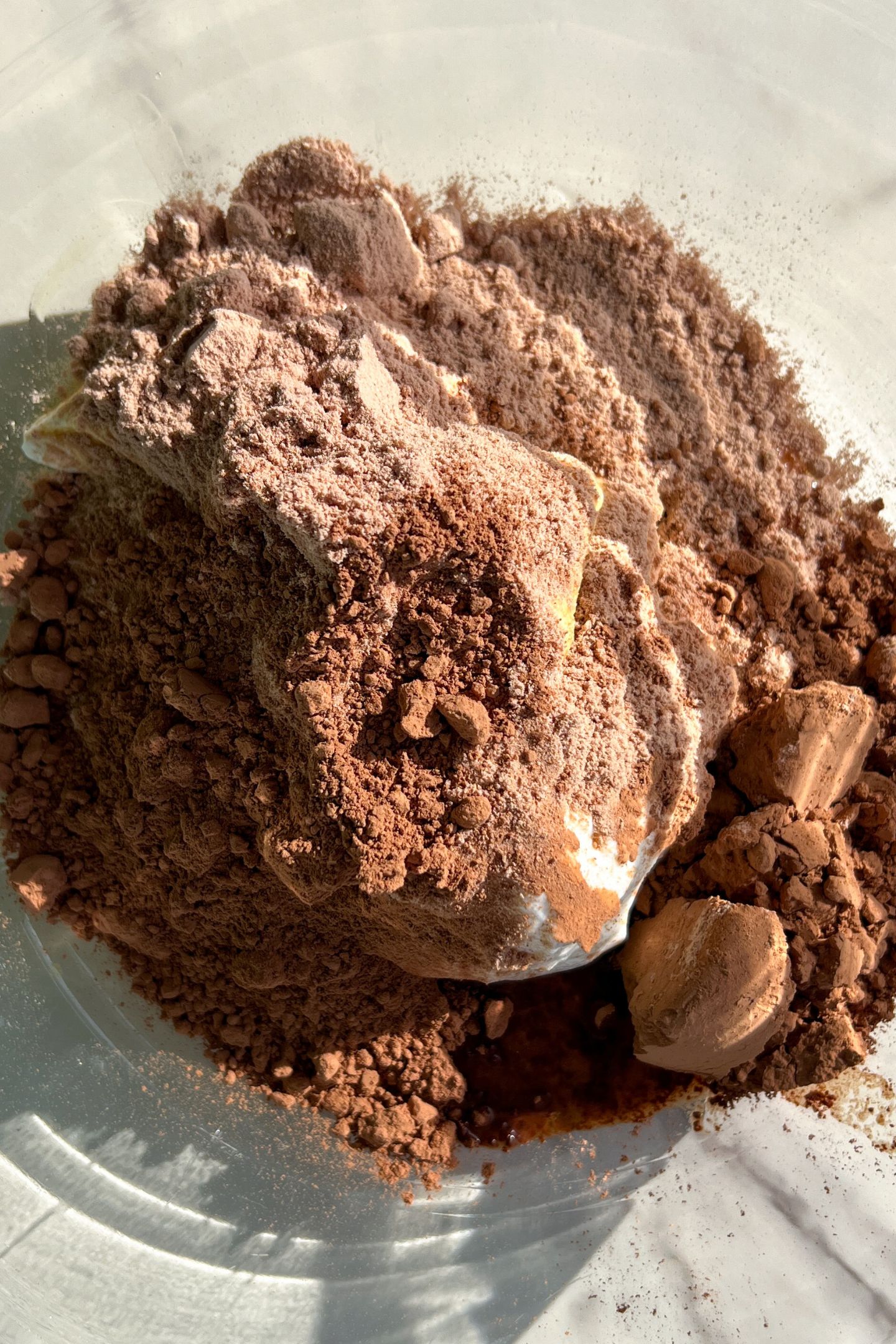 Wet ingredients in the mixing bowl topped with protein powder and cocoa powder.
