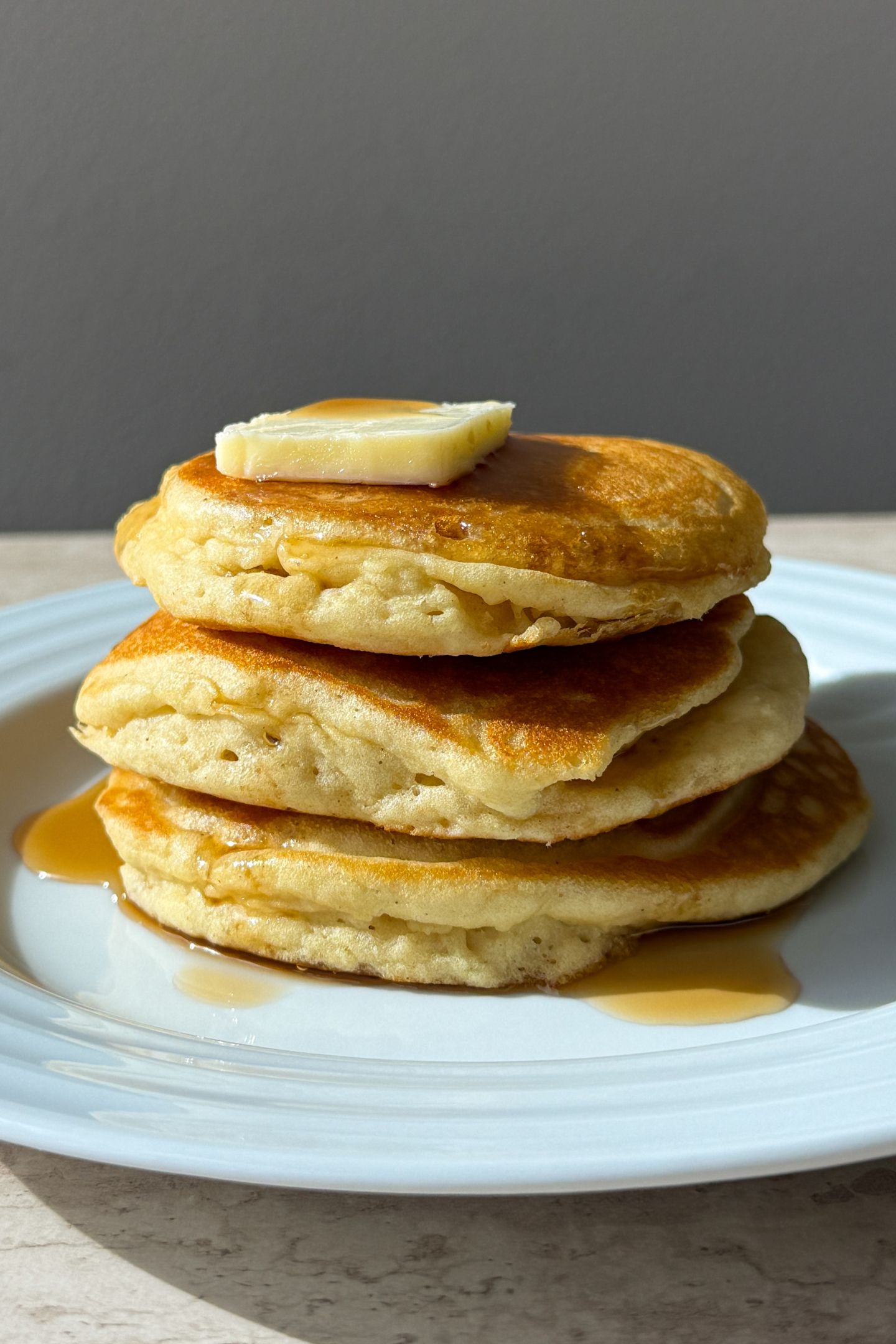 Stack of buttermilk pancakes topped with butter and syrup.
