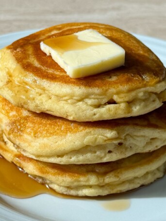 Stack of gluten-free buttermilk pancakes topped with butter and syrup.