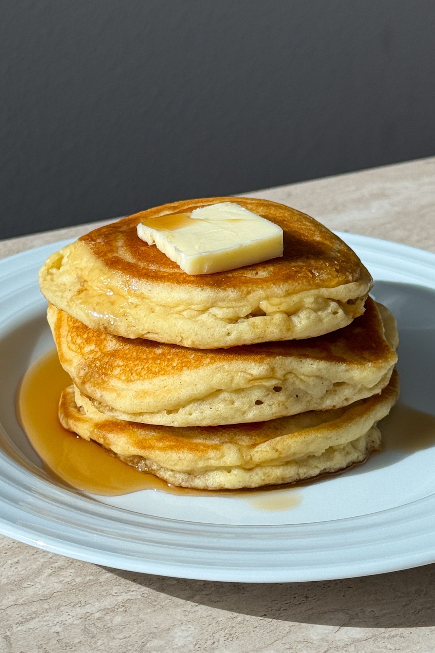 Stack of gluten free buttermilk pancakes topped with butter and maple syrup.