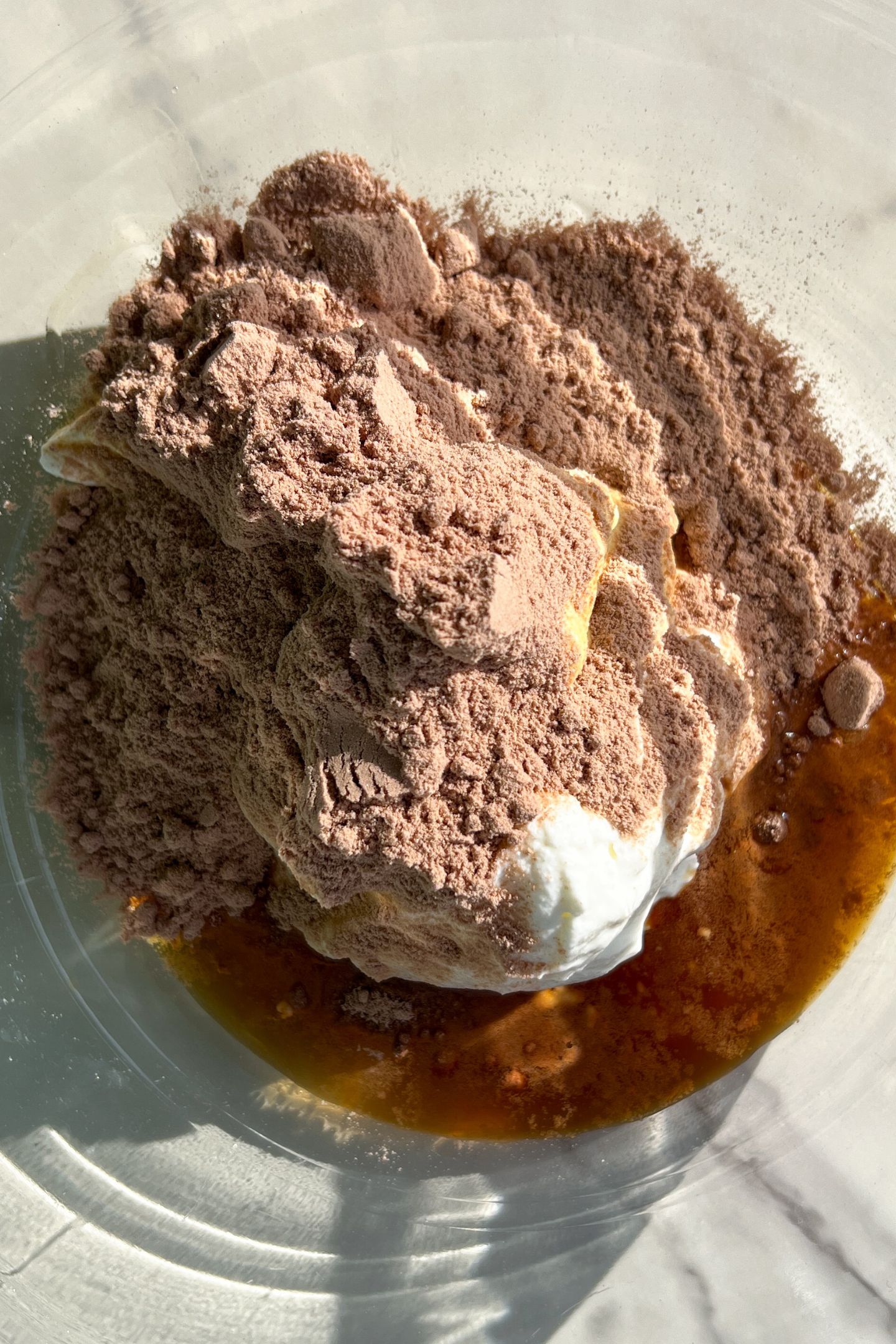 Wet ingredients in the mixing bowl topped with protein powder.