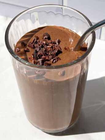 Chocolate smoothie topped with cacao nibs in a tall glass.