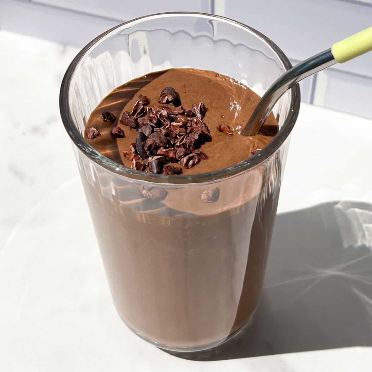 Chocolate smoothie topped with cacao nibs in a tall glass.