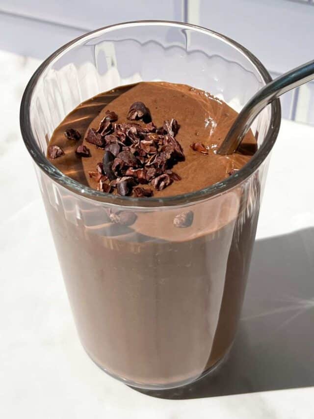 Chocolate smoothie topped with cacao nibs in a tall glass.