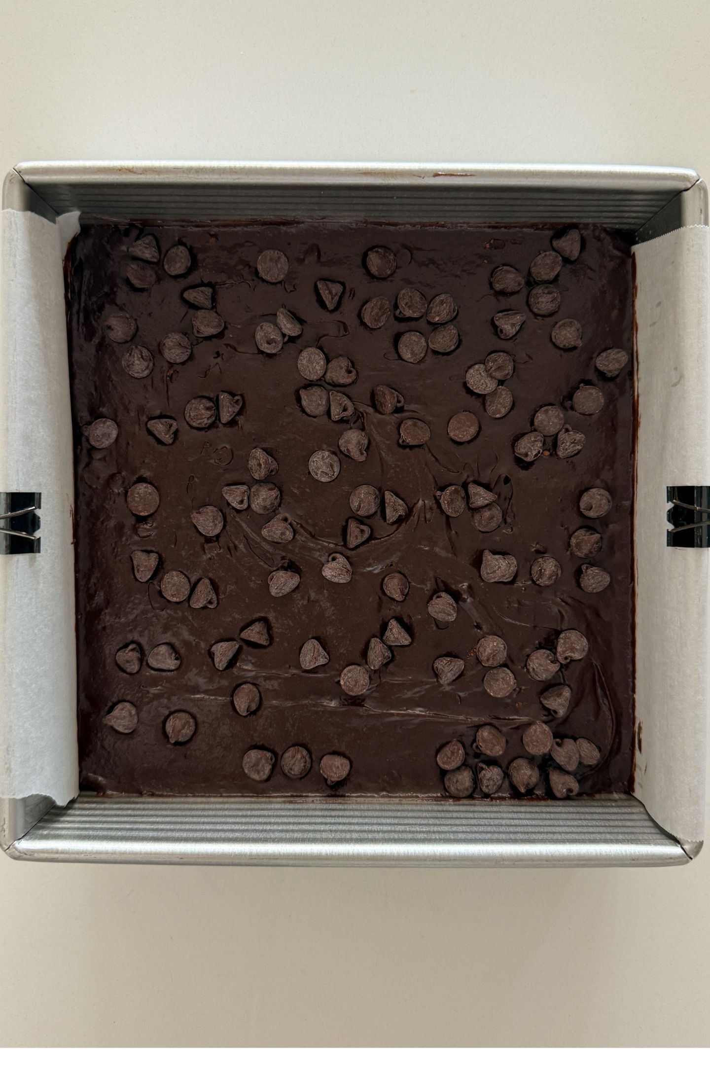 Brownie batter spread out in a square baking pan and topped with chocolate chips.