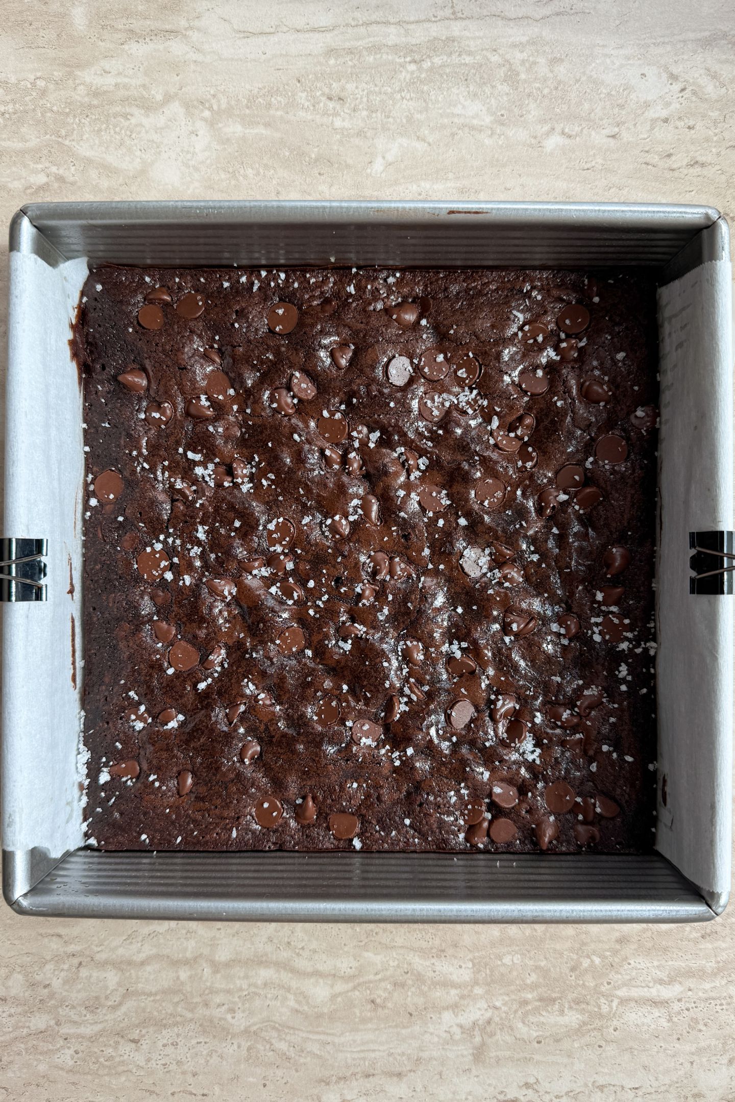 Baked espresso brownies topped with sea salt flakes in a square baking pan.