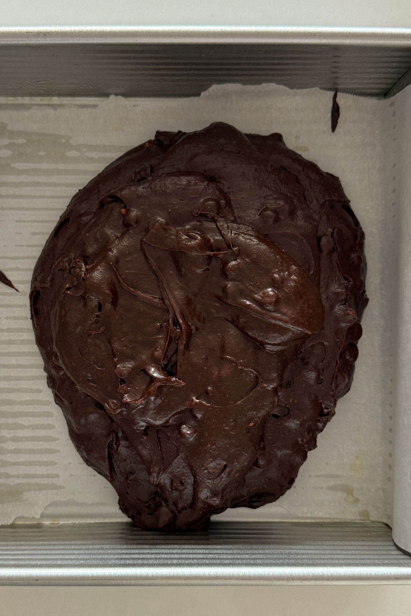 Brownie batter being poured into a square baking pan.