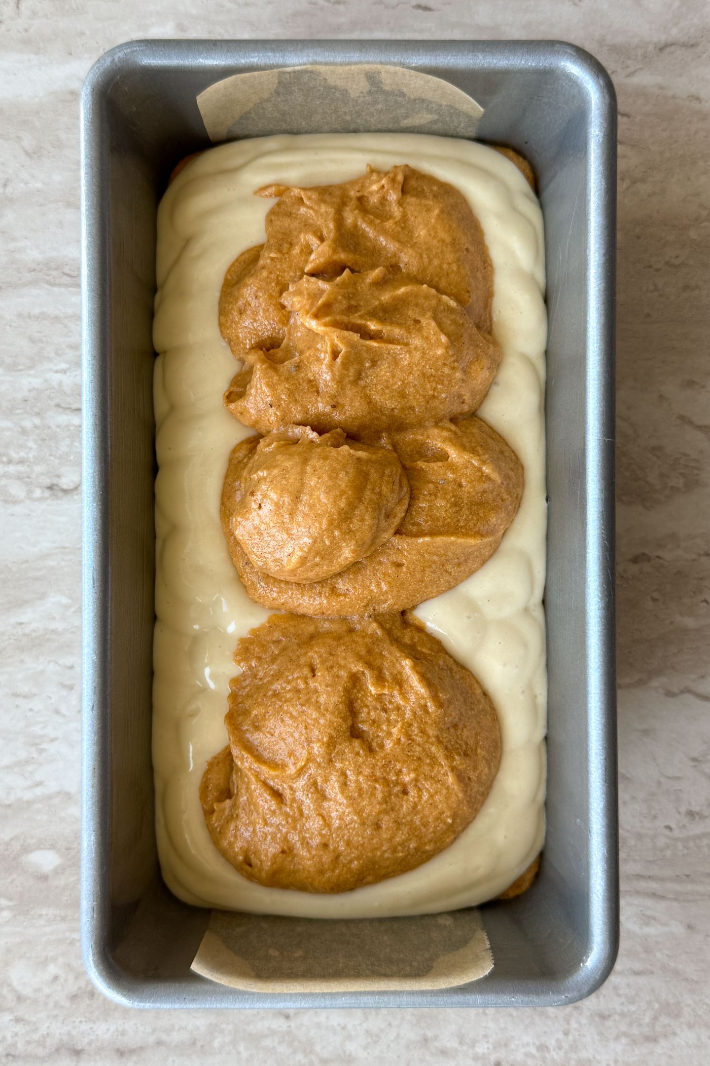 Adding cheesecake layer on top of pumpkin bread batter to the loaf pan.