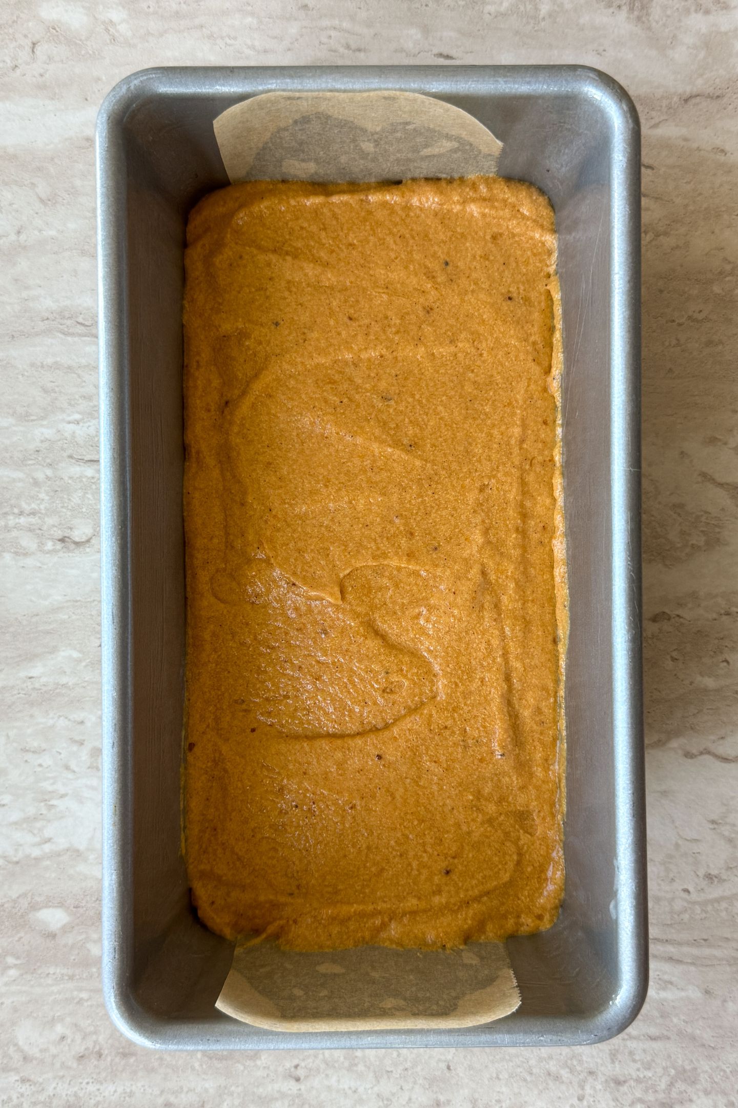 Adding pumpkin bread batter to the loaf pan.