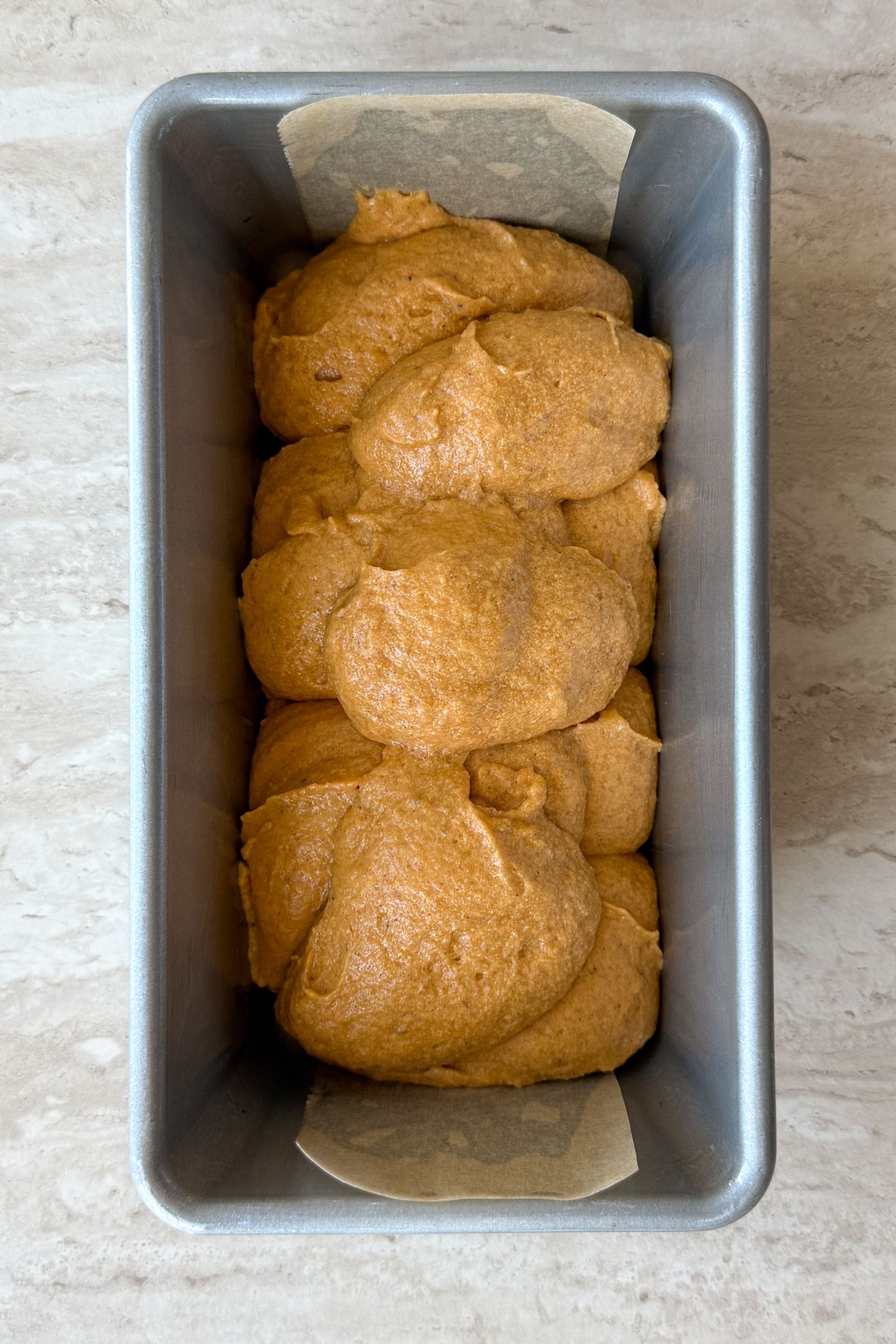 Adding pumpkin bread batter to the loaf pan.