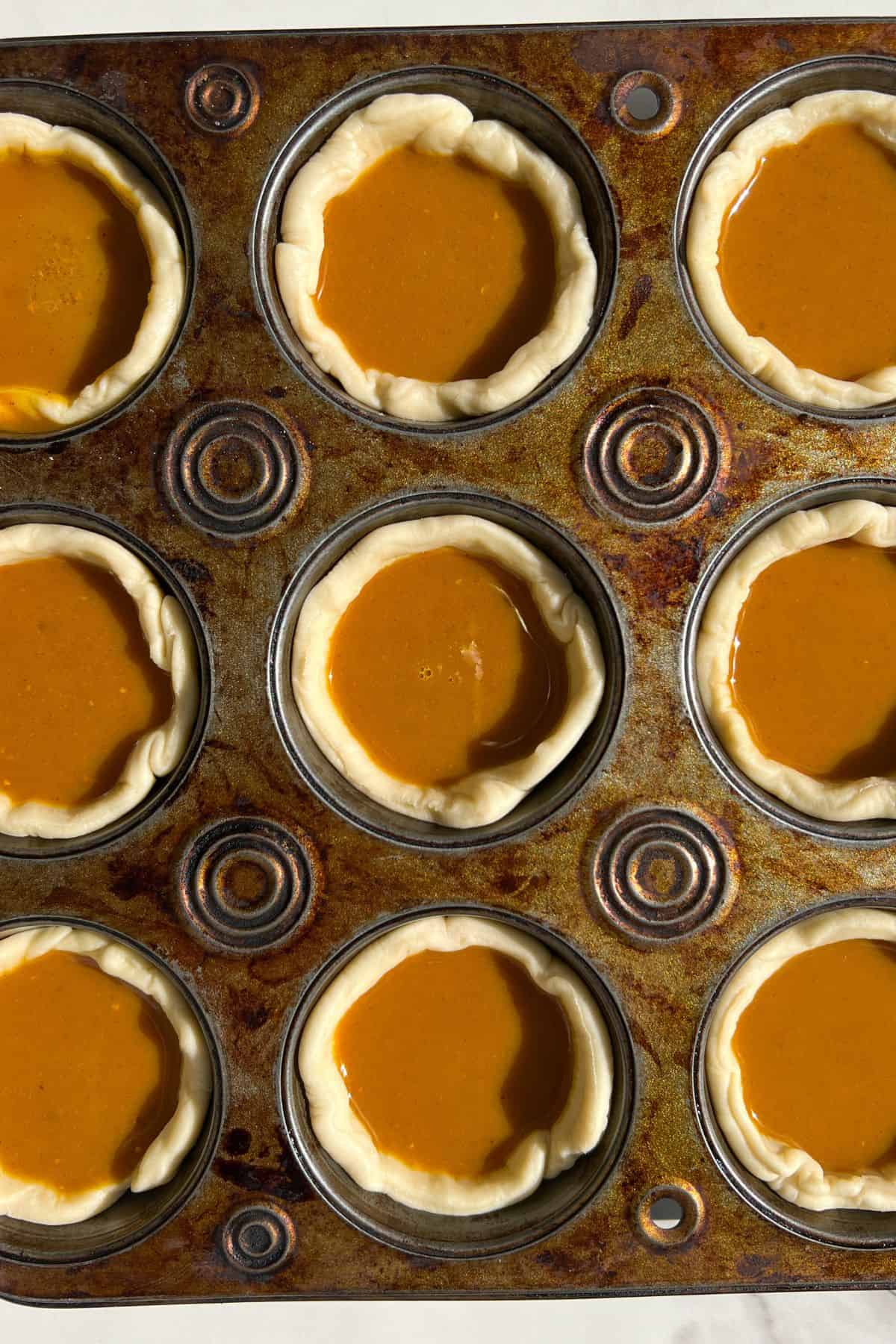 Unbaked mini pumpkin pies ready to go in the oven in a muffin tin.