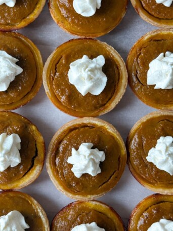 Mini Pumpkin Pies lined up on a platter and topped with homemade whipped cream.