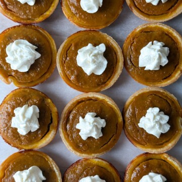 Mini Pumpkin Pies lined up on a platter and topped with homemade whipped cream.