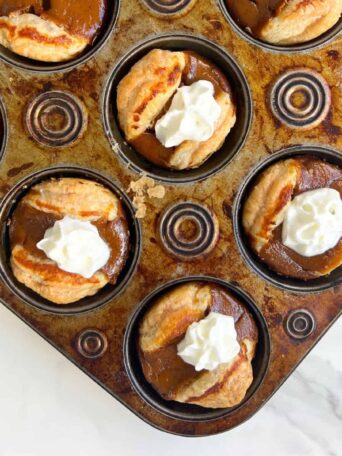 Mini Pumpkin Pies with Puff Pastry in a muffin tin and topped with whipped cream.