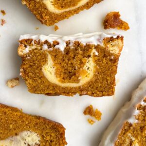 Slice of cheesecake filled pumpkin bread with cream cheese frosting on a platter.