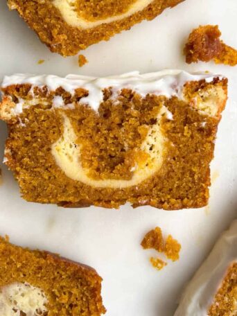 Slice of cheesecake filled pumpkin bread with cream cheese frosting on a platter.