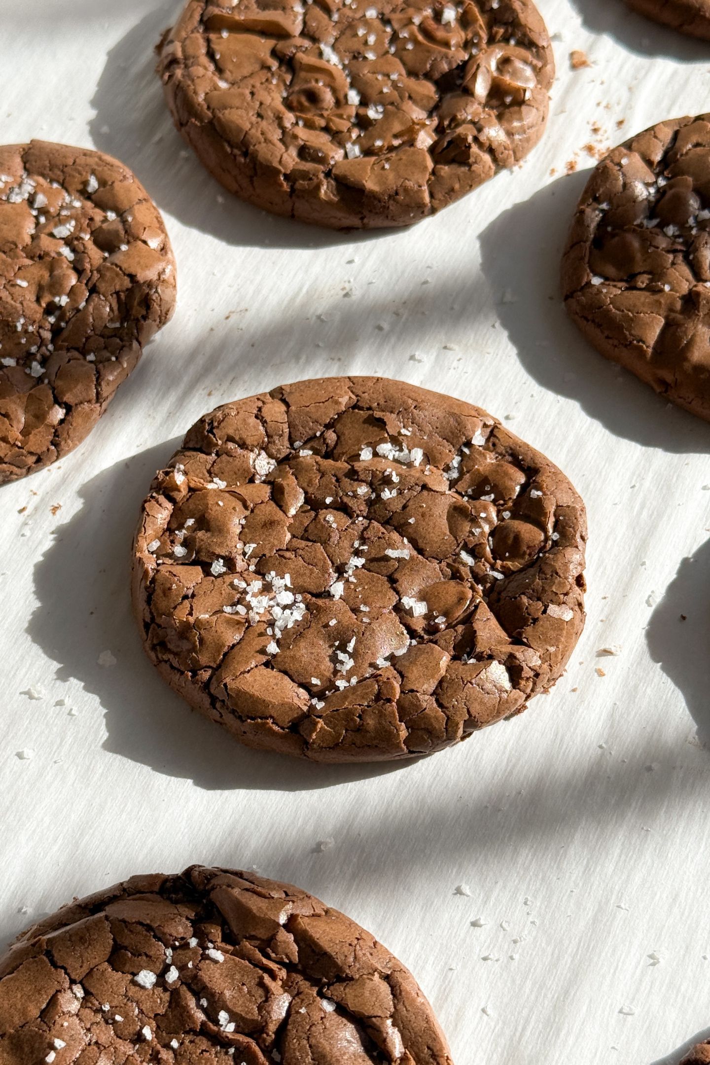 Baked brownie cookies on parchment paper and topped with sea salt flakes.