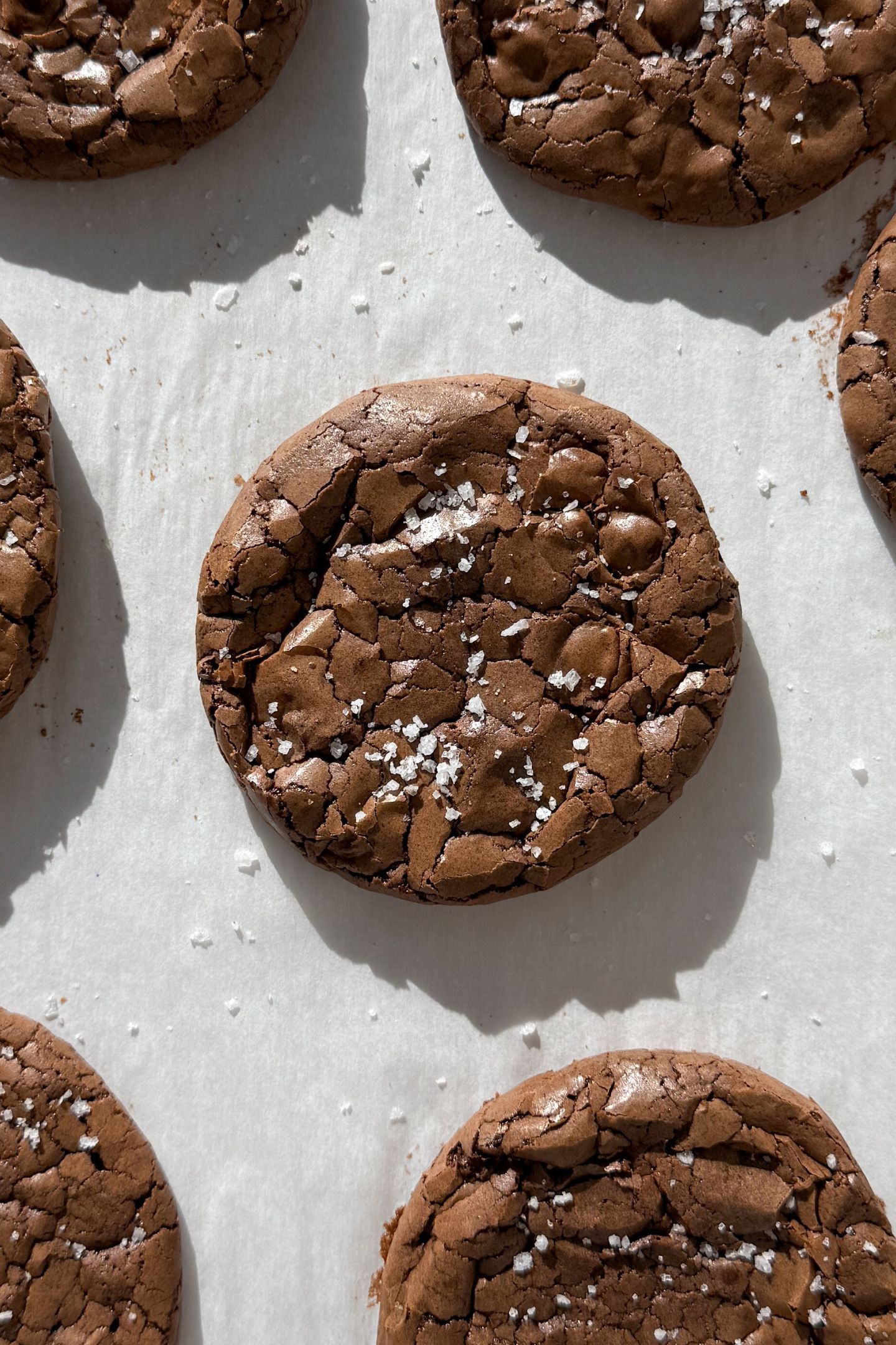 Fudge brownie cookies topped with sea salt flakes on baking sheet.