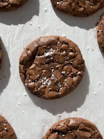 Fudge brownie cookies topped with sea salt flakes on baking sheet.