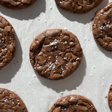 Fudge brownie cookies topped with sea salt flakes on baking sheet.