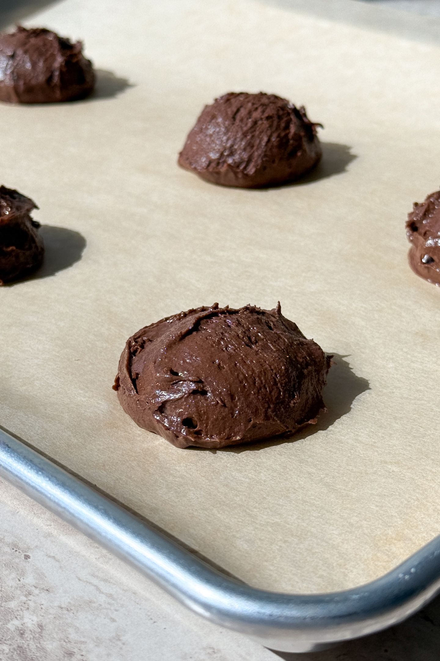 Brownie cookie batter portioned out on the cookie sheet that is lined with parchment paper.