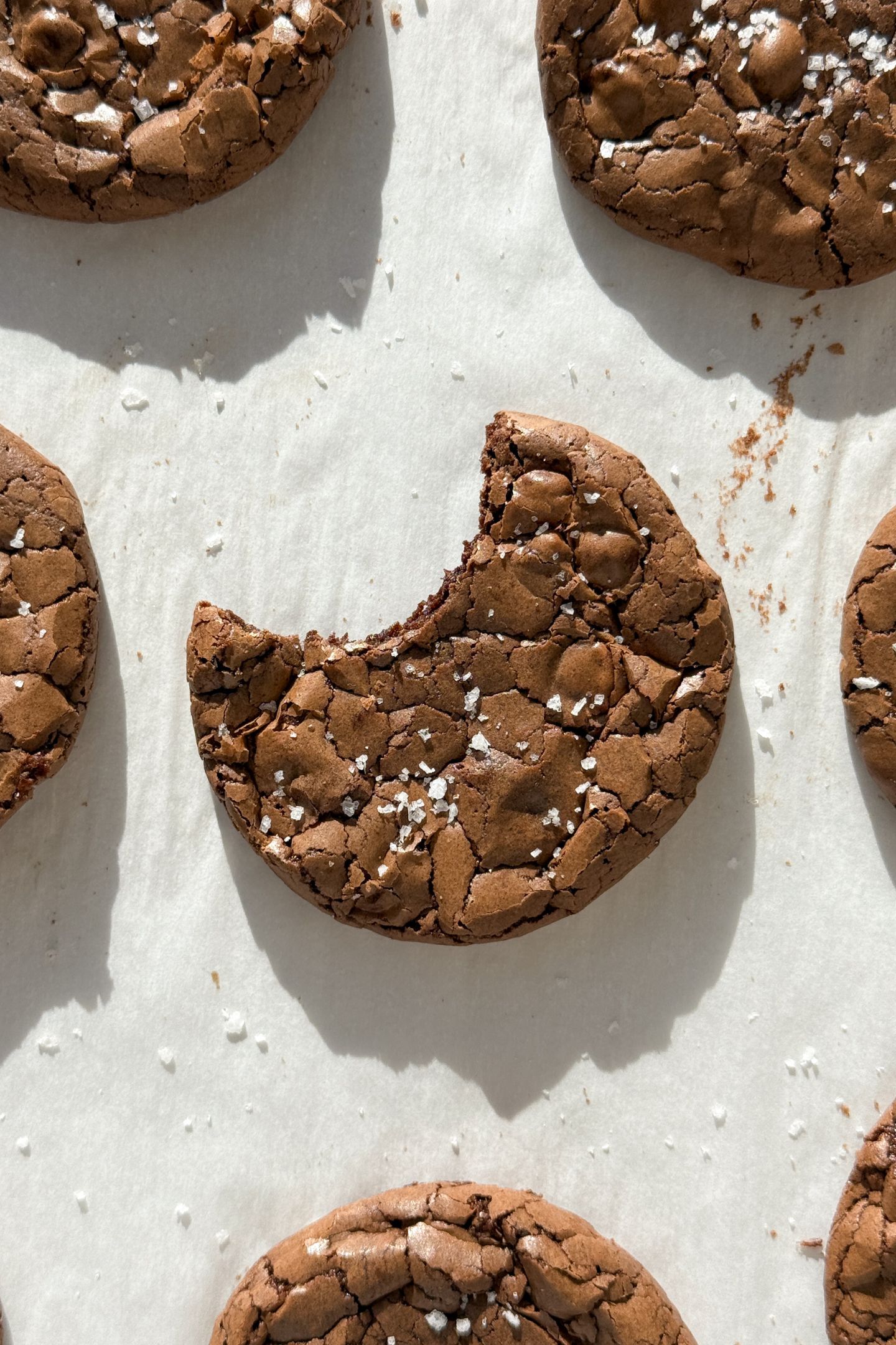 A brownie cookie on parchment paper with a bite taken out of it.