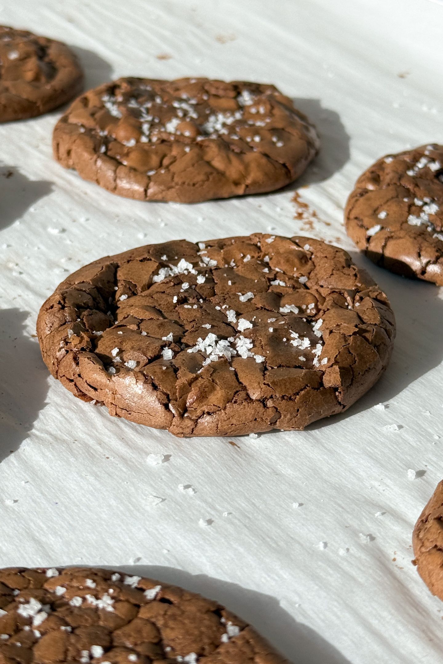 Baked brownie cookies on parchment paper and topped with sea salt flakes.