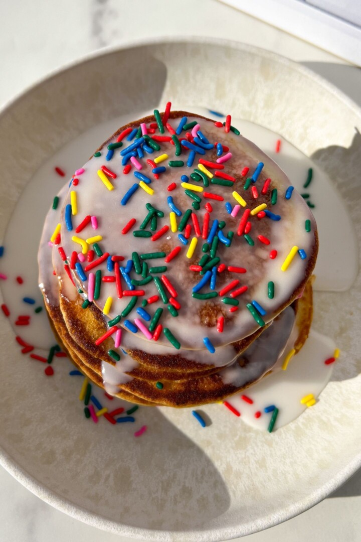 Birthday cake pancakes topped with a glaze and sprinkles.