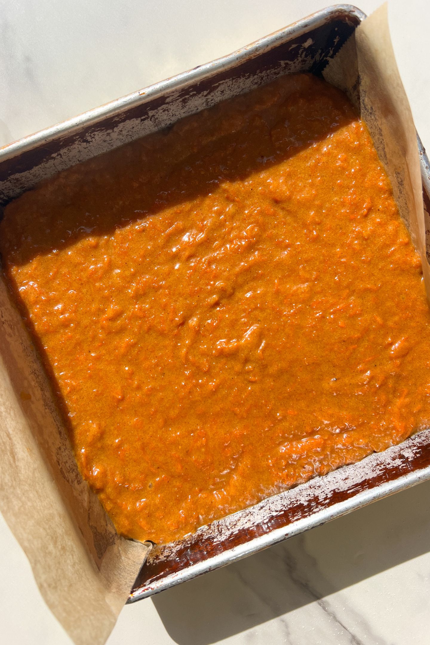 Carrot cake batter in a baking pan lined with parchment paper.