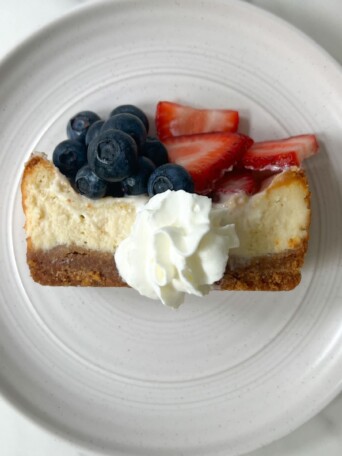 Vanilla Cheesecake bar on a plate with whipped cream and fruit.