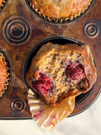 Blackberry Banana Oatmeal Muffins with a bite taken out of it sitting in a muffin tray.